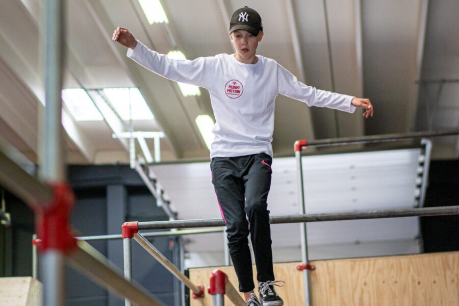 Een jongen die over een stang balanceert op hoogte in een freerunhal