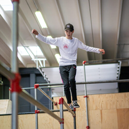 Een jongen die over een stang balanceert op hoogte in een freerunhal